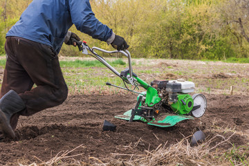 Fototapeta na wymiar A man works in the garden with the help of a motoblock. Loosening the soil with a cultivator