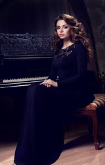 Beautiful thoughtful girl sitting near piano. Fashion studio portrait