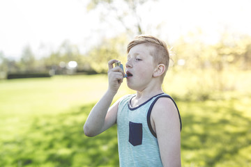 Boy using an asthma inhaler in the park