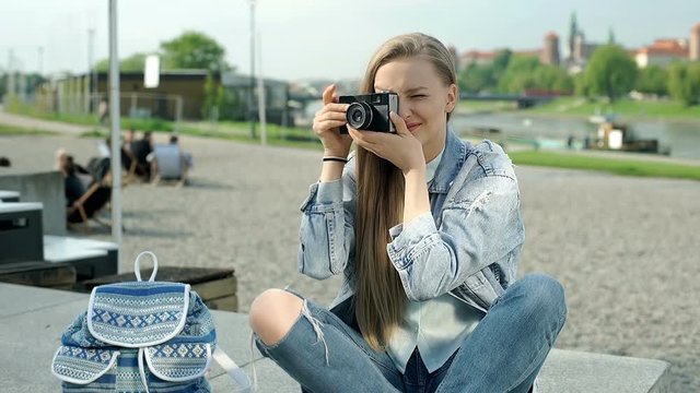 Beautiful girl doing photos on old camera and smiling outdoors

