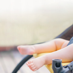 Close-up of baby sleeping in stroller outdoors. Small baby barefoot with copy space