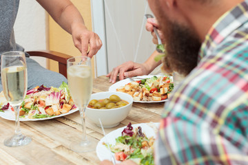 Friends having informal dinner on wooden table on terrace outdoor. Close-up shot