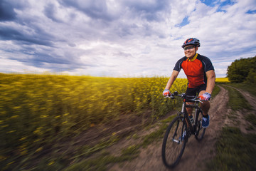 Fototapeta na wymiar A male cyclist is riding on a picturesque yellow rapeseed field.