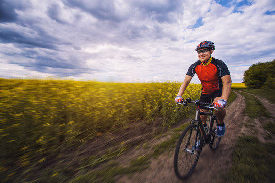 A male cyclist is riding on a picturesque yellow rapeseed field.