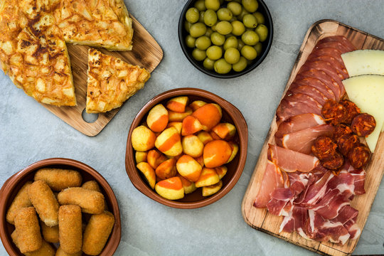Traditional spanish tapas. Croquettes, olives, omelette, ham and patatas bravas on gray stone
