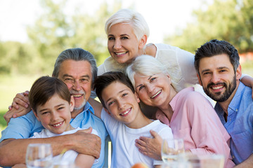 Family sitting at table outdoors, smiling
