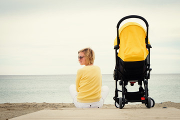Young mother relaxing on beach with baby stroller outdoor. Back view