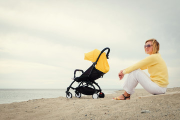 Mother gets some rest on beach while baby sleeping in stroller with copy space