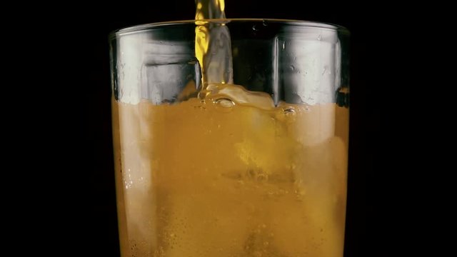 Slow mo. Filled glass with orange drink with ice cubes juice soda on black background