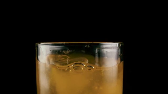 Slow motion. In a full glass of orange juice drink throw ice cube black background