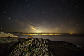Night landscape in the sea, sky filled with stars and city lights in the distance. Ustica, Sicily