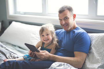 father and daughter relax in bed with tablet computer