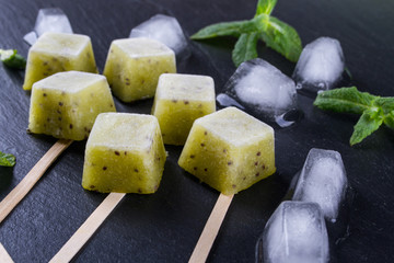 Homemade natural popsicles made with fresh kiwi with mint leaves. Summer Ice Cream, fruit dessert on  the black slate board