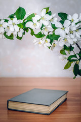 A closed book on the table with a branch of apple blossoms