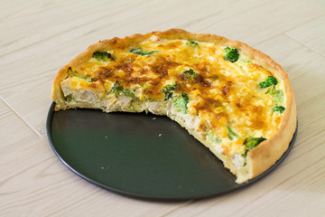 Traditional French quiche Lorraine with chicken, egg, milk, cheese broccoli and corn on a wooden background.