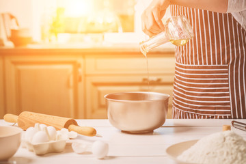 Young woman pouring oil into a bowl with dough, close-up