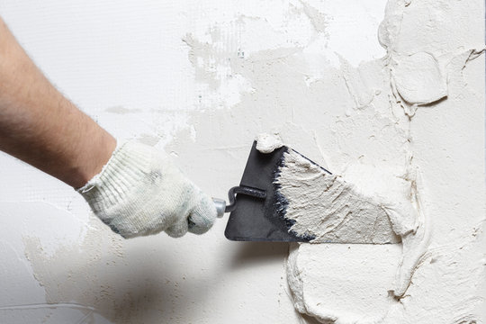 Construction worker puts a gypsum on the wall with a spatula