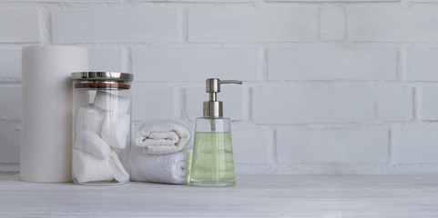 Part of spa interior. Cotton napkins, cotton pads, tissue, towels, soap and cosmetic products on a wooden table. White  background and table. Copy space. Selective focus. Wide panoramic image.