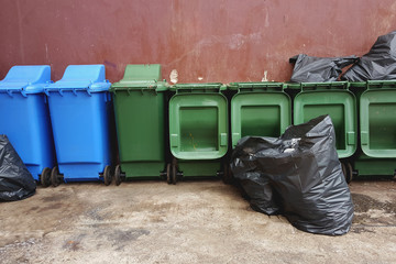 green and blue plastic recycle bins and  black garbage bags on red wall background