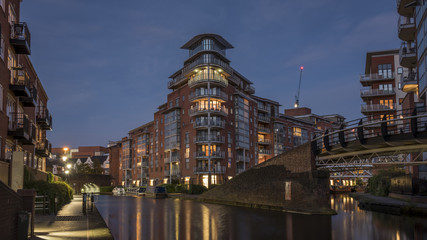 Modern apartment buildings, lit up at dusk, overlooking an urban waterway, canal, in Birmingham, England, UK