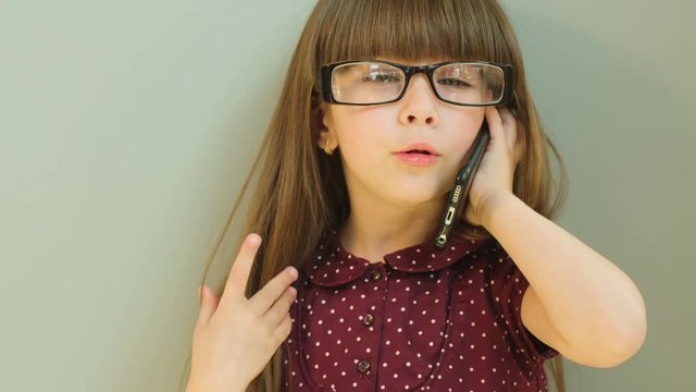 Portrait shot og little girl talking on the cell phone, wearing big office glasses. Close up. Grey background