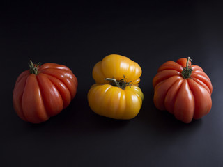 Three big red and yellow beef tomatoes with green stems isolated on black background