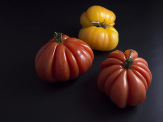 Obraz premium Three big red and yellow beef tomatoes with green stems isolated on black background