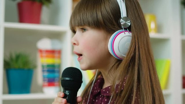 Cute Little Girl Emotionaly Singing On Black Microphone At Home. Close Up