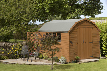 A Dutch barn style garden shed with a patio in a English country garden