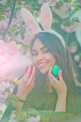 woman smiling with colored eggs and rosy bunny ears, sakura