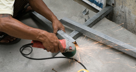 COLOR PHOTO OF WORKER CUTTING STEEL WITH ELECTRIC WHEEL GRINDER
