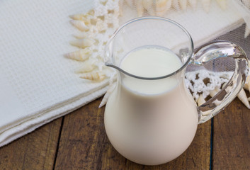 Milk in glass milk jug close up on rustic wooden background with lace jug cover and white kitchen cloth