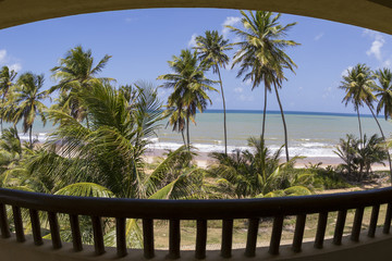 beach and blue sea seen from the balcony of a resort hotel room with coconut palm trees and waves...