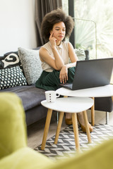 Fototapeta premium Young woman with curly hair, uses laptop and sitting on the sofa at home