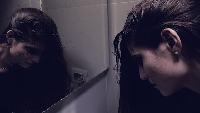 Desperate young woman in bathroom looking in mirror crying thinking about suicide  slow motion
