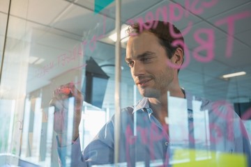 Male executive writing on glass board with a marker