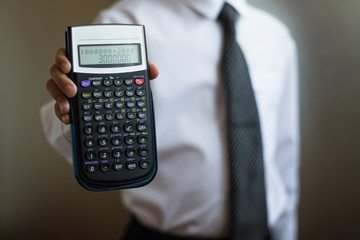 Young businessman in a white shirt and tie with a calculator in his hand. The boy shows a calculator with a figure of 3000000