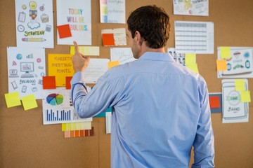 Male executive pointing at bulletin board in office
