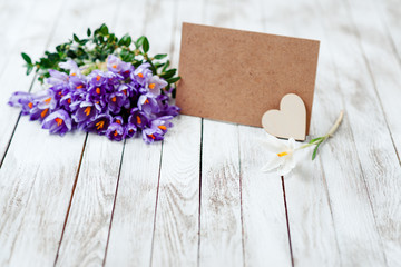 Beautiful crocus flowers in a basket near empty card for your text on wooden background.