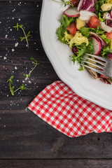 Fresh salad with mixed greens, radish, cheese and tomato in a plate on wooden background. Italian Mediterranean or Greek cuisine. Vegetarian vegan food