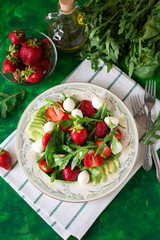 Fresh vegetarian salad with spinach, arugula, avocado slices, strawberries and mini mozzarella on green wooden table. Selective focus