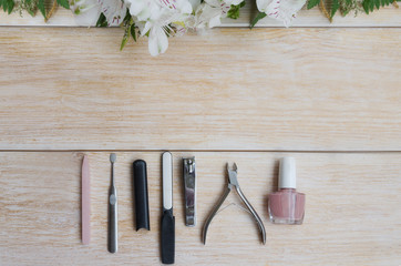 Fototapeta na wymiar Manicure and pedicure accessories on wooden background with flower frame. Diamond nail file, stone file cuticle remover, nail clipper and nude nail polish.Copy space.