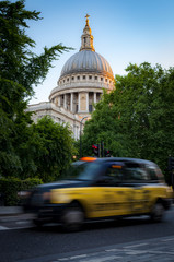 Fototapeta na wymiar Taxi cab passing by the english landmark that is St Paul's Cathedral surrounded by trees with green leafs in London, England, UK