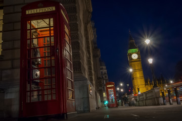 Traditional red phone booth or telephone box with the Big Ben in the background, possible the most famous English landmark, at night in London, England, UK