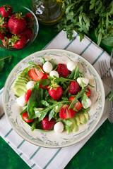 Fresh vegetarian salad with spinach, arugula, avocado slices, strawberries and mini mozzarella on green wooden table. Selective focus