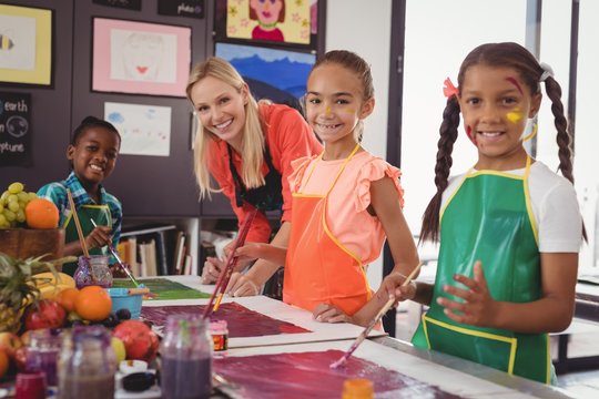 smiling teacher and schoolkids standing in drawing classroom