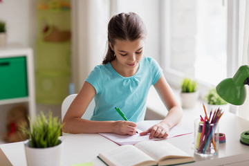 happy girl with book writing to notebook at home