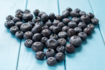Freshly picked blueberries in shape of the heart on blue wooden background