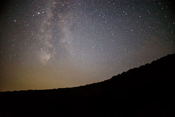 A clear night sky with a hill and trees in the foreground