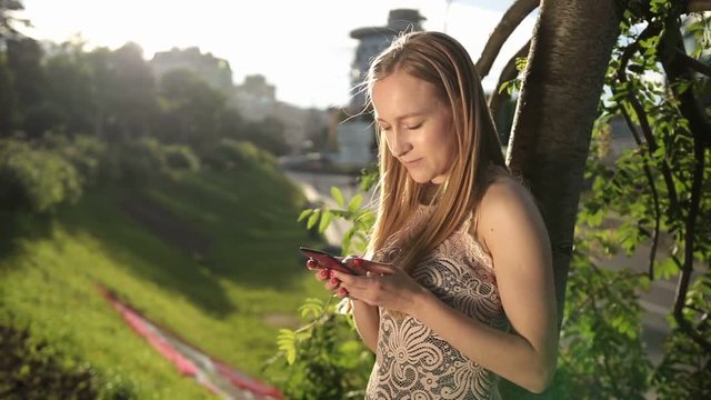 Joyful woman texting on smartphone in park